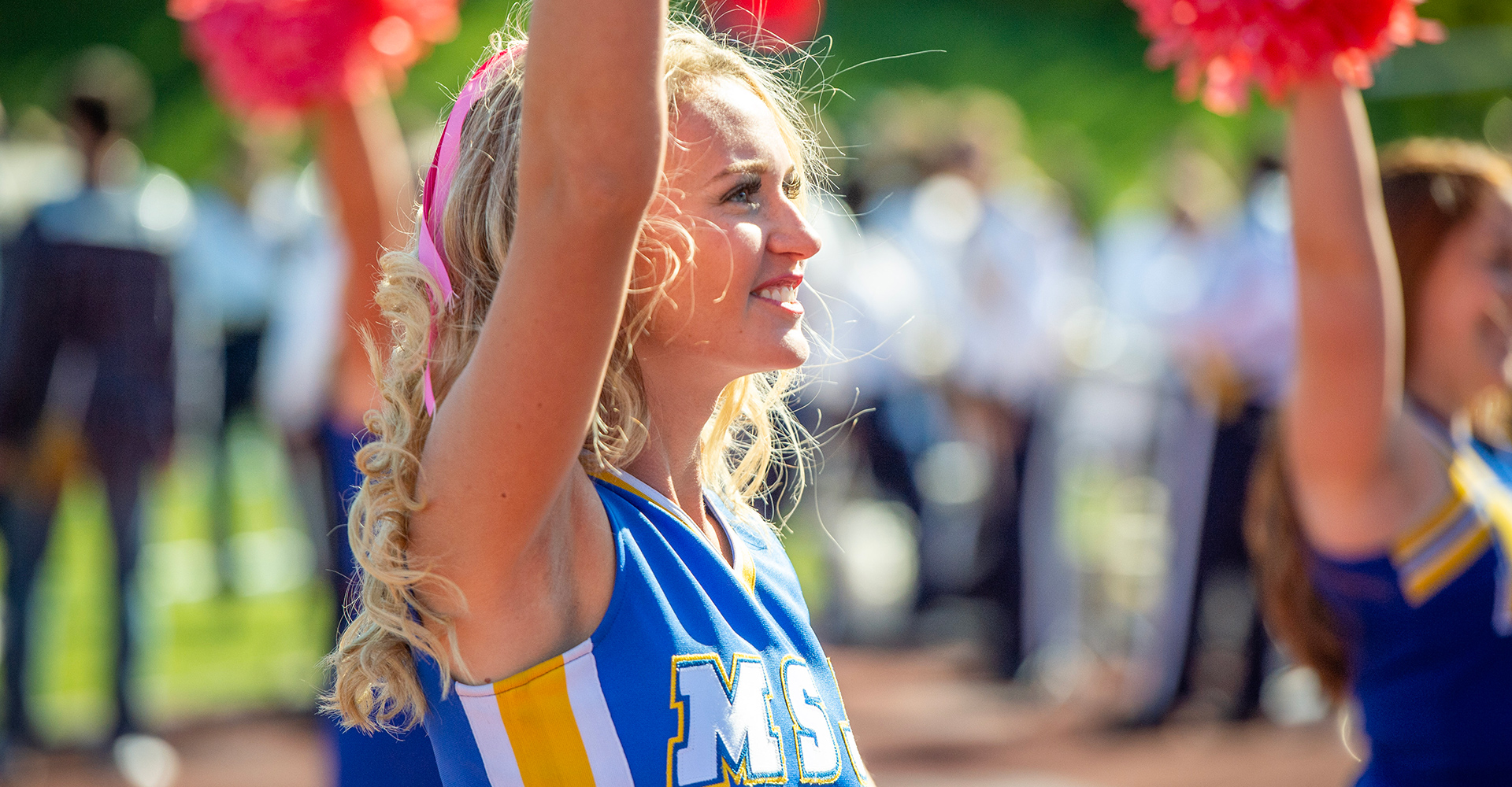 MSJ cheerleader raising arm with pom-pom in Schuler Field.