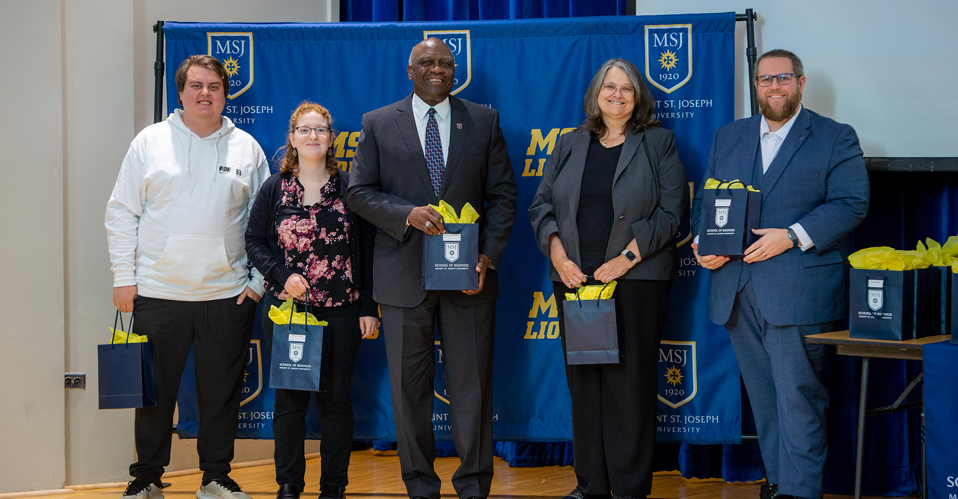 msj president and staff standing with gift bags at high school business competition