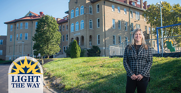 Mount St. Joseph alumna angela frith standing next to St. Rita's school of the deaf smiling.