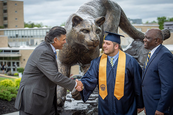 Three men shake hands in front of a lion statue
