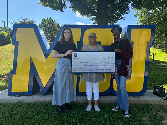 students in front of msj letters with giant check
