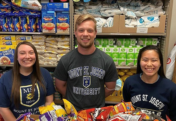 Mount St. Joseph food pantry volunteers standing by pantry smiling.