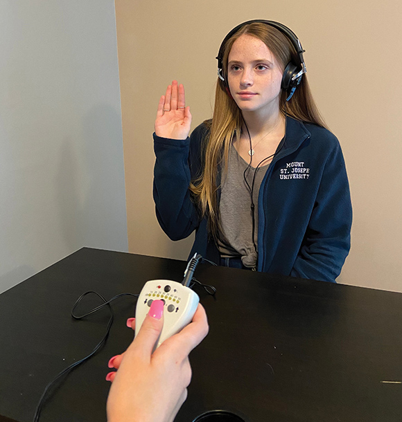 Speech, Language, and Hearing student with headphones lifting hand for hearing test.