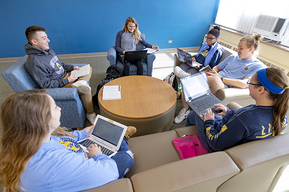 students gathered around a table with laptops